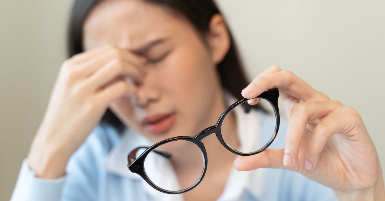 Woman experiencing eye strain and holding her glasses resembling does wearing glasses make your eyesight worse